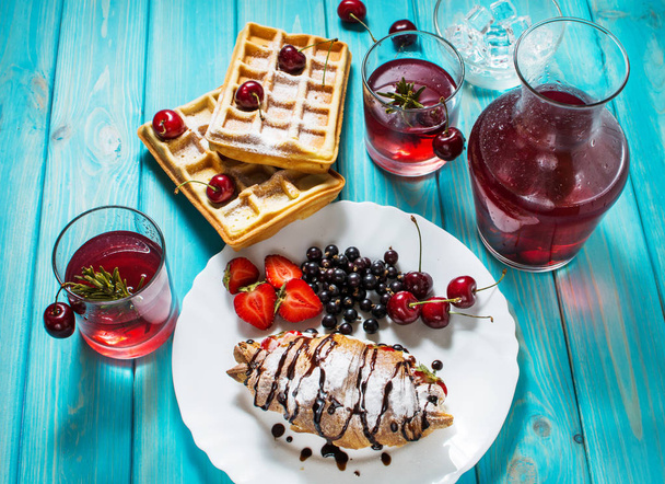 Aamiainen: vohvelit ja croissant mustikoilla, kirsikoilla ja mansikoilla. Haudutetut hedelmät lasit ja dekantteri
. - Valokuva, kuva