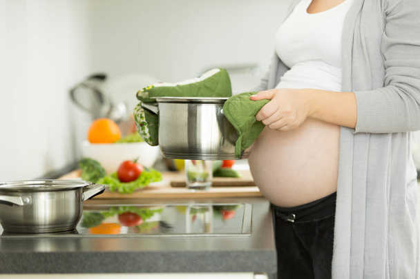 Pregnant woman posing on kitchen while cooking soup - Фото, изображение
