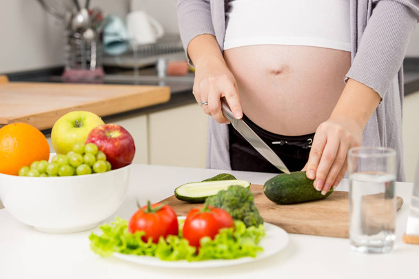 Closeup photo of pregnant woman making salad on kitchen - Photo, Image
