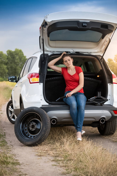 Sad woman sitting in open trunk of broken car on the road - Photo, image