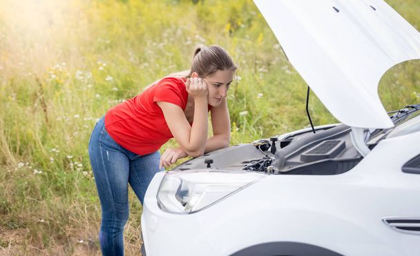Młoda kobieta, patrząc na silnik uszkodzony samochód w dziedzinie - Zdjęcie, obraz