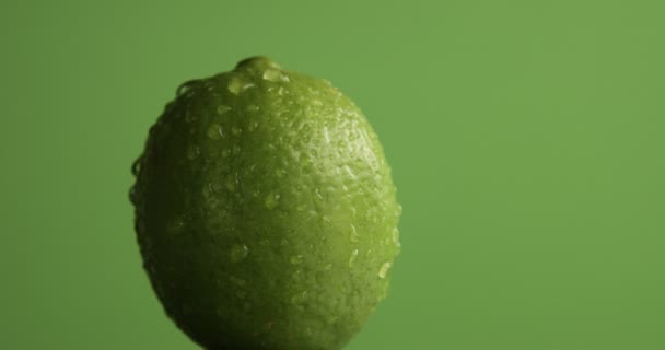 lime turning on its axis on green background covered by water drops - Filmagem, Vídeo