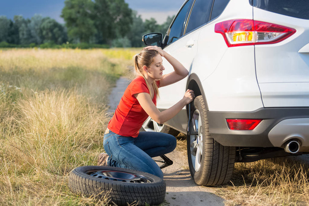 Triste femme remplaçant pneu de voiture à plat au champ
 - Photo, image