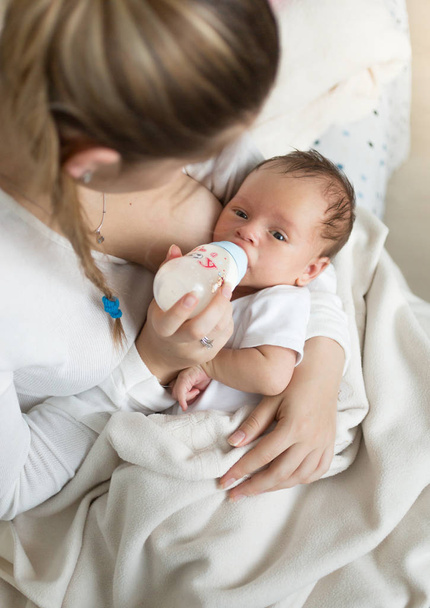 Nahaufnahme Porträt einer jungen Mutter, die ihr Baby mit Milch von Bot füttert - Foto, Bild