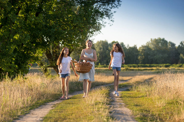 Щасливі дівчата гуляють з матір'ю на сільській дорозі
 - Фото, зображення