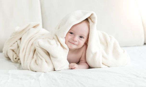 Rozkošný chlapeček sedí na posteli a kryjí v deku - Fotografie, Obrázek