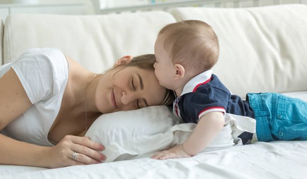 Portrait of cute baby boy lying with young mother on bed - Photo, Image
