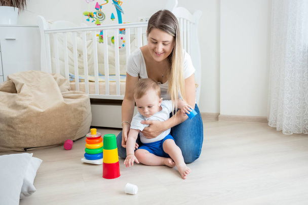 Mother looking at her baby boy assembling toy pyramid on floor a - Photo, Image