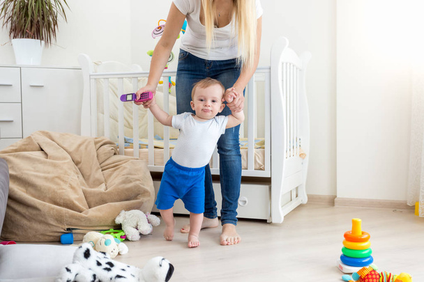 Mother holding baby boy by hands and walking at living room - Foto, imagen