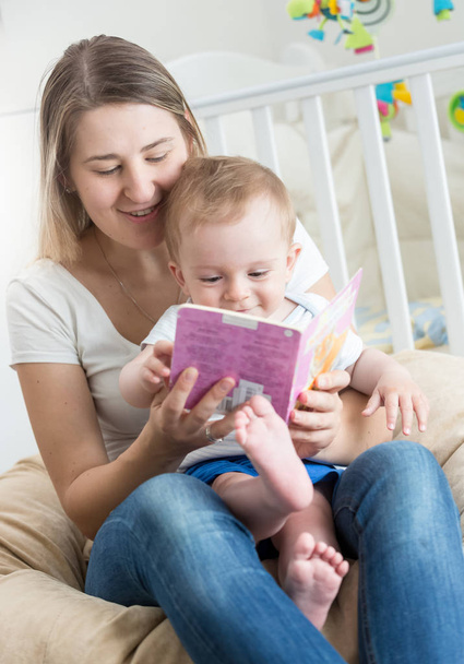 Portret van babyjongen zit op moeders schoot en lezen van boek - Foto, afbeelding