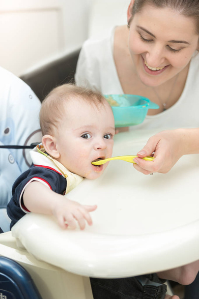 Lächelnde junge Mutter füttert ihr Baby im Hochstuhl - Foto, Bild