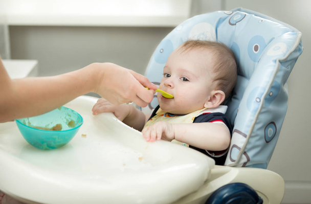 Closeup of mother giving porridge from spoon to her baby - Fotó, kép