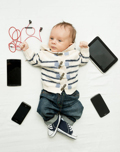 Schattige kleine jongen liggend op bed met digitale tabletten en smartphone - Foto, afbeelding