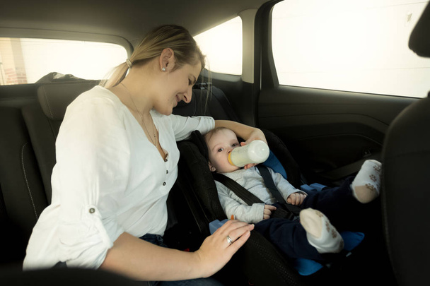 Retrato de la madre alimentando al bebé en el asiento de seguridad del automóvil
 - Foto, imagen