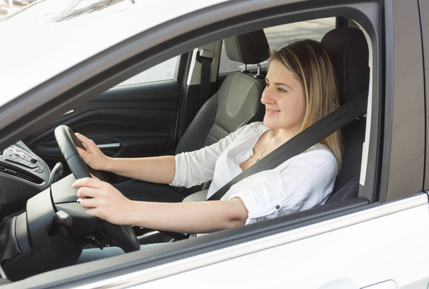 Молодая улыбающаяся женщина водит машину и смотрит на дорогу
 - Фото, изображение