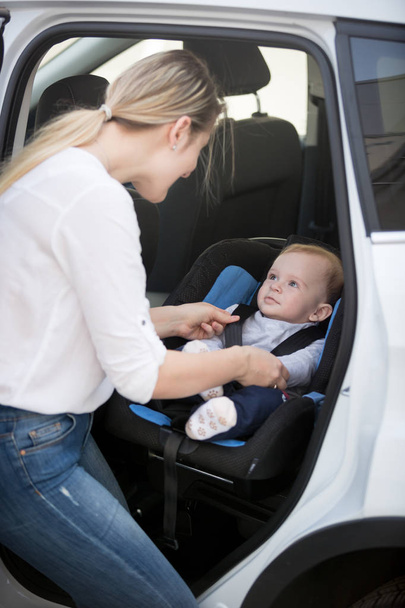 Madre sentando a su bebé en el asiento de seguridad del coche
 - Foto, imagen