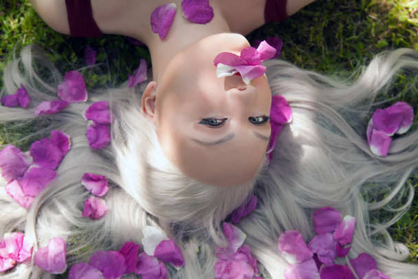 pretty young woman lying on the grass with pink petals - Photo, Image