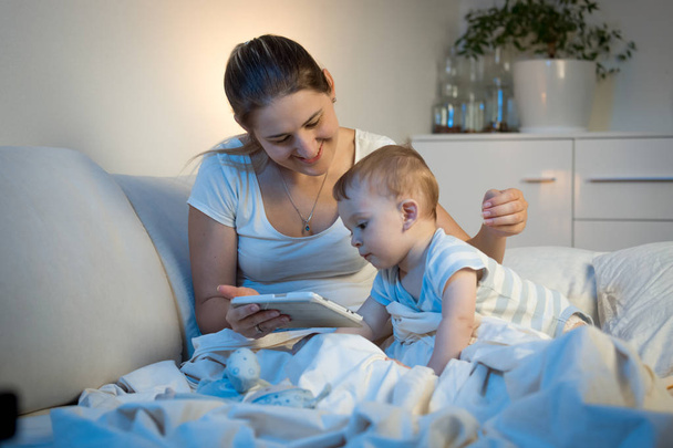 Bébé garçon assis sur le lit avec la mère et en utilisant une tablette numérique à
  - Photo, image