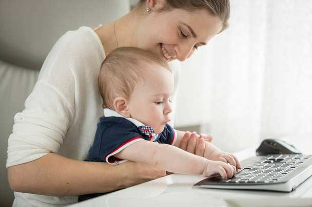 Niedliches Baby sitzt auf dem Schoß der Mutter und tippt auf der Tastatur - Foto, Bild
