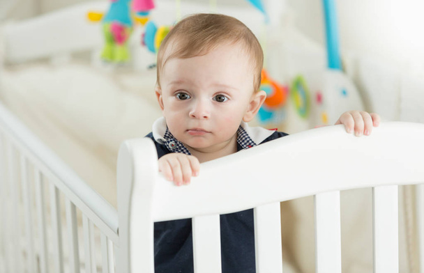 Beautiful 9 months old baby boy standing in white crib - Foto, Imagem