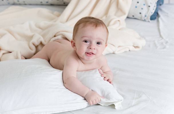 Sorrindo bebê deitado em travesseiros na cama grande
 - Foto, Imagem