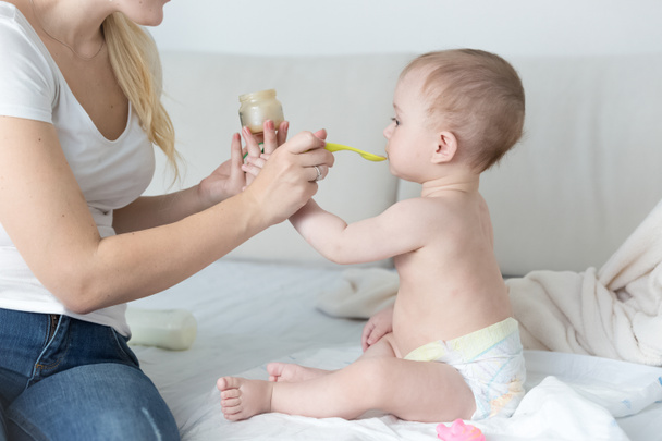 Mother feeding her adorable baby boy on bed with fruit sauce fro - Фото, зображення
