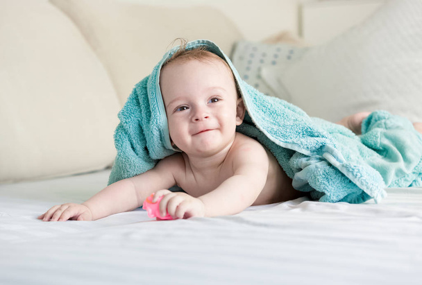 Onnellinen hymyilevä vauva sinisen pyyhkeen alla indeksoi sängyllä valkoisella s
 - Valokuva, kuva