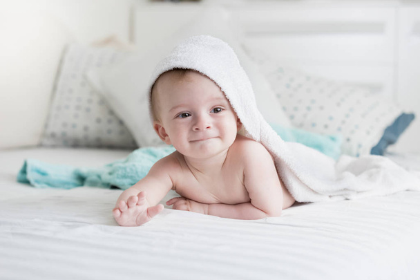 9 Monate altes Baby liegt unter weißem Handtuch auf Bett - Foto, Bild