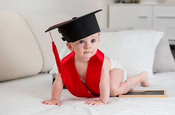 Adorable 10 months old baby boy in graduation cap crawling - Photo, Image