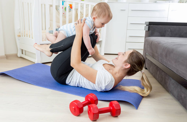 Mother with baby doing yoga exercise on floor at living room - Fotografie, Obrázek