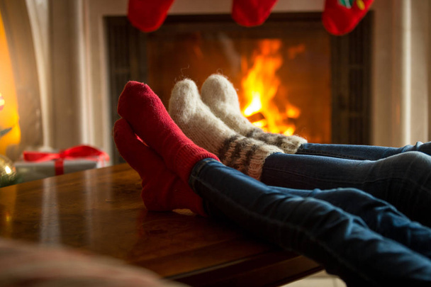 Los pies de la familia en calcetines de lana se calientan cerca de la chimenea en llamas en
 - Foto, Imagen