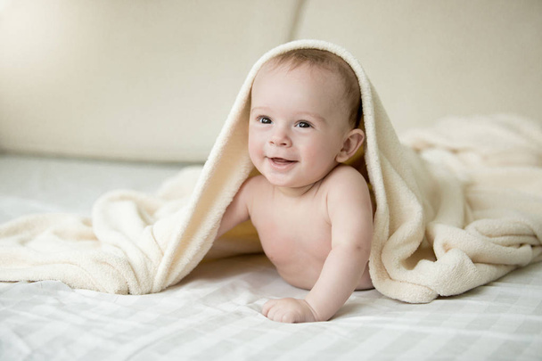 Portret van verrast jongetje onder deken op bed liggen - Foto, afbeelding