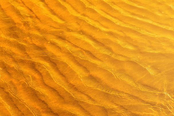 Luz dourada refletindo uma onda de água no mar e areia no pôr do sol. Tom de ouro puro
 - Foto, Imagem