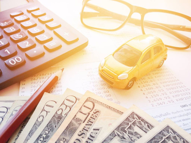 Modelo de carro em miniatura, lápis, dinheiro, calculadora, óculos e caderneta de conta poupança ou ficha financeira em fundo branco
 - Foto, Imagem