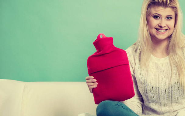 Woman sitting on couch holding hot water bottle - Foto, afbeelding