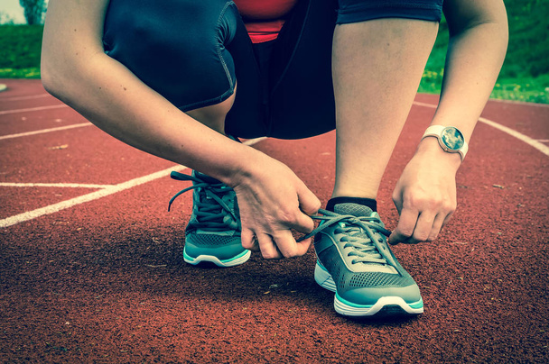 Woman is lacing her shoes on a stadium running track - Photo, Image