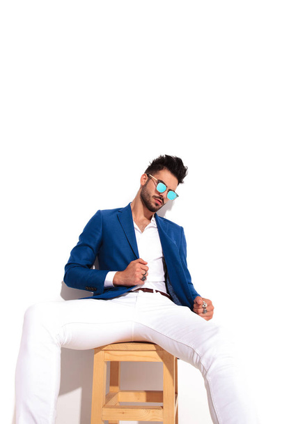άνθρωπος των επιχειρήσεων μόδας στα γυαλιά ηλίου, κάθεται και κρατώντας το κοστούμι του co - Φωτογραφία, εικόνα