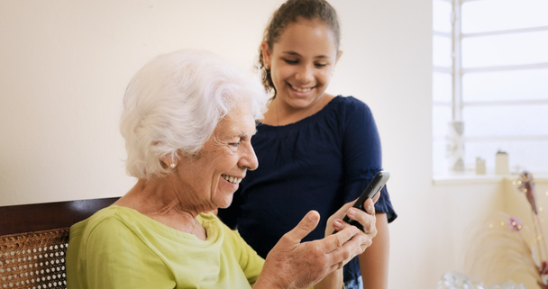Девушка помогает пожилой женщине с помощью мобильного телефона и технологии
 - Фото, изображение