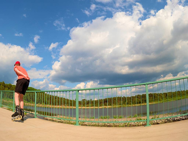 Vista trasera al patinador en línea en camiseta roja y pantalones negros patinando en el puente. Patinaje en línea exterior
  - Foto, imagen