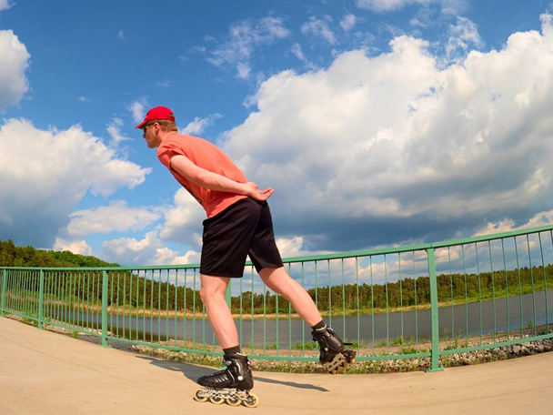 Vista trasera al patinador en línea en camiseta roja y pantalones negros patinando en el puente. Patinaje en línea exterior
  - Foto, Imagen