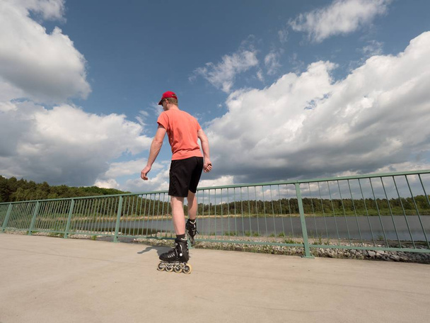 Κυλίνδρου σκέιτερ σε δράση. Ο άνθρωπος βόλτα σε inline πατίνια βόλτα κατά μήκος περιπάτου κουπαστή, ουρανό στο παρασκήνιο - Φωτογραφία, εικόνα