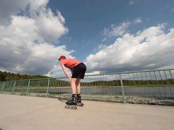 Middle age man in red t-shirt  with inline skates ride in summer park, popular outdoor skating.  - Photo, Image