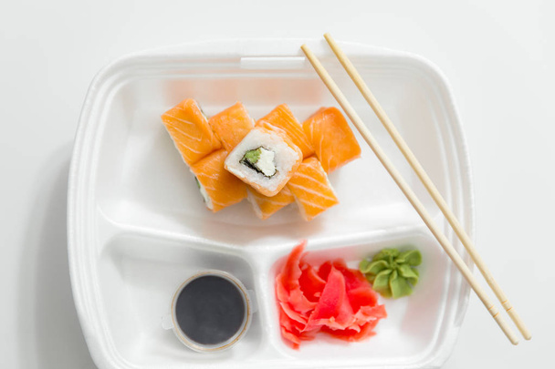 rollo con palillos, rollos, sushi. palillos, jengibre, salsa de soja en la entrega del envase sobre fondo blanco
 - Foto, Imagen