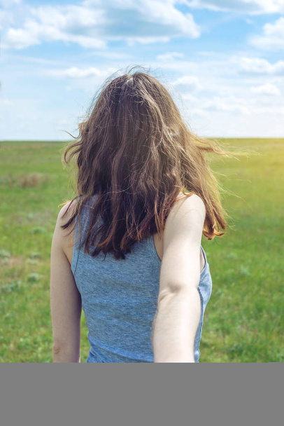 Siga-me, menina morena atraente segurando a mão das pistas em um campo verde limpo, estepe com nuvens
 - Foto, Imagem