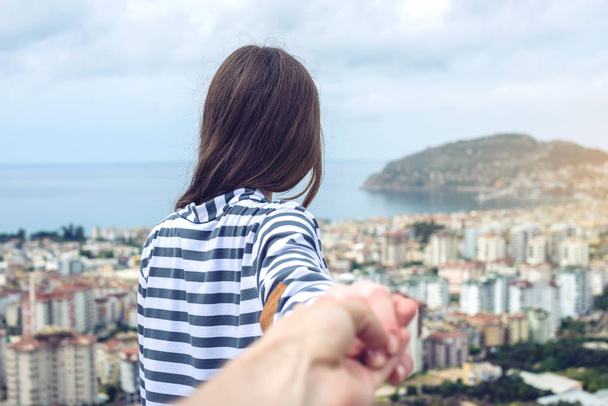 Follow me, Attractive brunette girl holding the hand leads into the coastal city from a height - Photo, Image