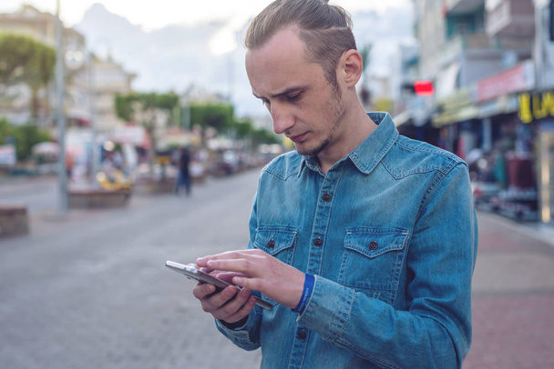 Чоловік мандрівник дивиться на свій смартфон на тлі вулиць міста
 - Фото, зображення