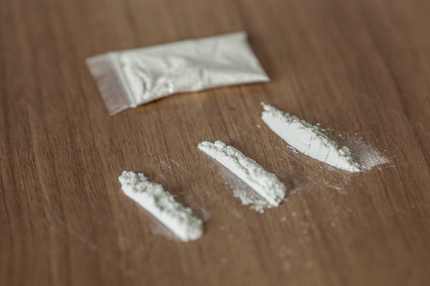 γραμμές και πλαστικό πακέτο της κοκαΐνης στο ξύλινο τραπέζι - Φωτογραφία, εικόνα