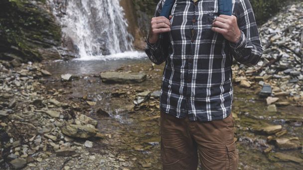 Hands Unrecognizable Man Holds Backpack Strap On Waterfall Background Hiking Journey Travel Trek Concept - 写真・画像
