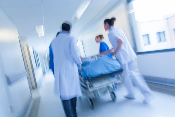 Una fotografía borrosa en movimiento de un paciente en camilla o camilla siendo empujado a velocidad a través de un pasillo del hospital por médicos y enfermeras a una sala de emergencias
 - Foto, imagen