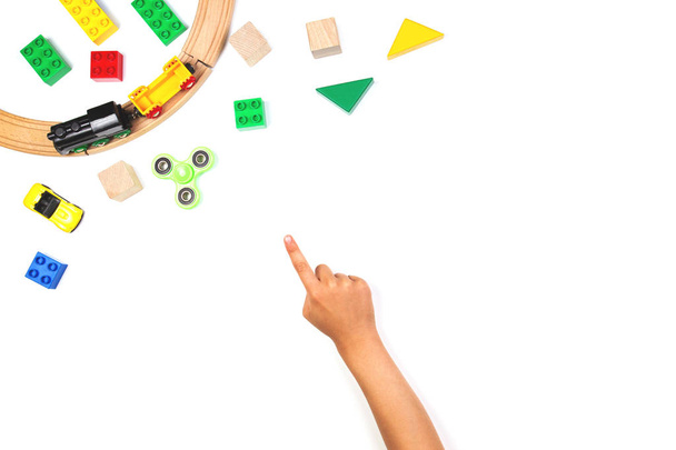 Niño señalando con el dedo a los juguetes de colores. Fidget spinner, coches, tren de juguete, ladrillos y bloques sobre fondo blanco
 - Foto, imagen